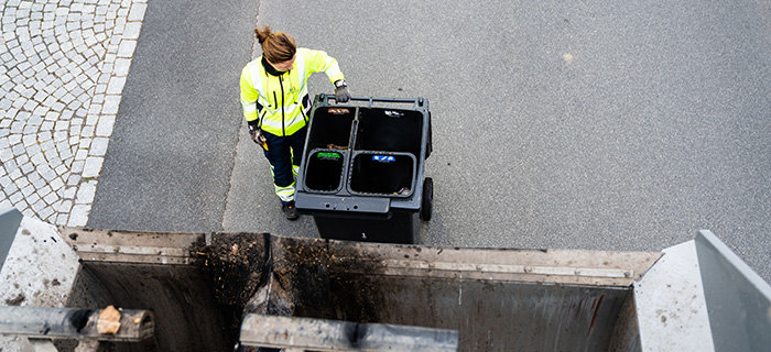 renhållningsarbetare står bakom en sopbil för att fästa ett fyrfackskärl för tömning
