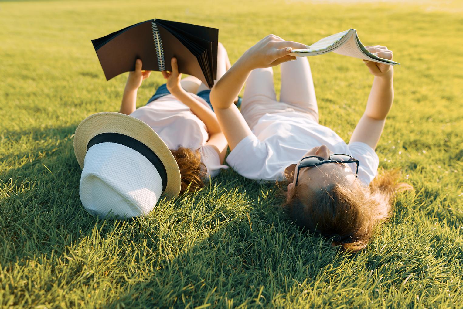 Barn ligger på rygg i gräset och läser