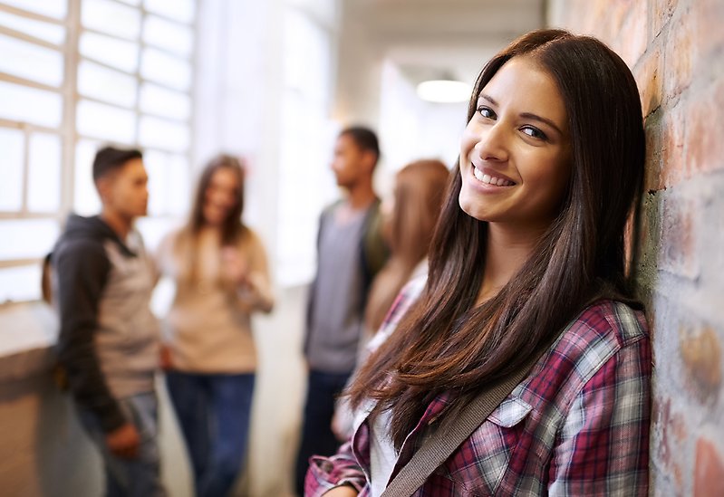 Bild på en grupp elever i en skolkorridor, med en brunhårig tjej i förgrunden.